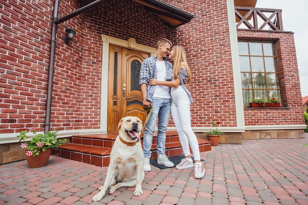 Atractiva pareja joven con labrador frente a su nueva y hermosa casa