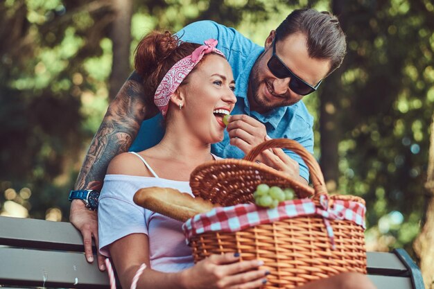 Atractiva pareja de mediana edad durante las citas, disfrutando de un picnic en un banco en el parque de la ciudad.