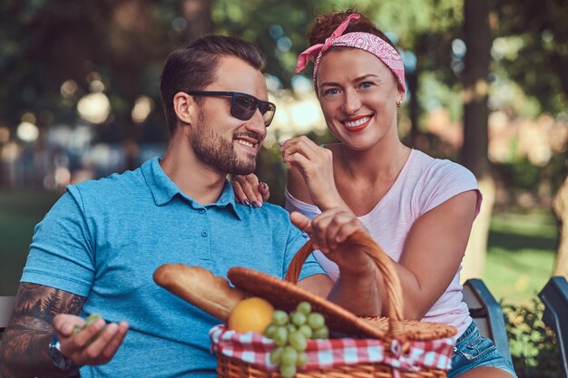 Atractiva pareja de mediana edad durante las citas, disfrutando de un picnic en un banco en el parque de la ciudad.