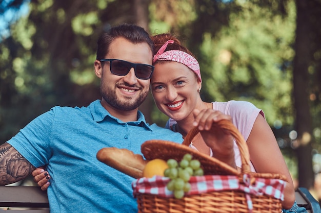 Atractiva pareja de mediana edad durante las citas, disfrutando de un picnic en un banco en el parque de la ciudad.