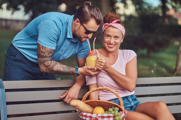 Atractiva pareja de mediana edad durante las citas, disfrutando de un picnic en un banco en el parque de la ciudad.