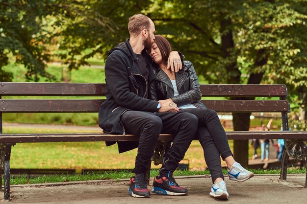 Atractiva pareja moderna abrazándose en un banco en el parque. Disfrutando de su amor y la naturaleza.