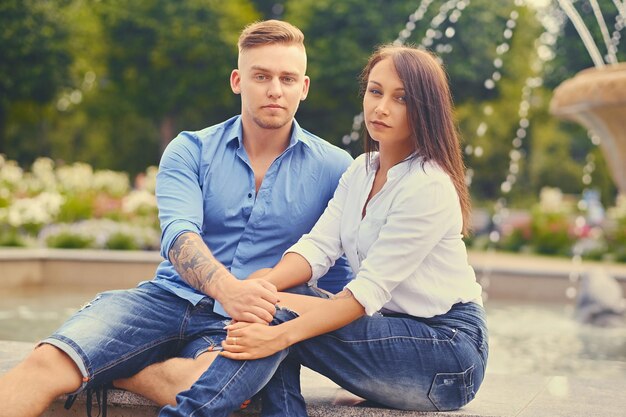 Atractiva pareja moderna en una cita está posando sobre la fuente de la ciudad.