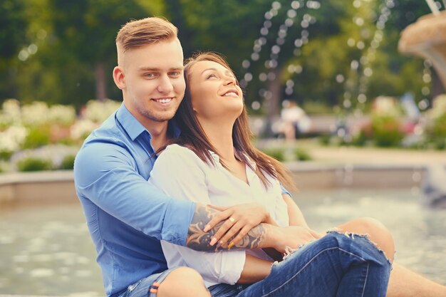 Atractiva pareja moderna en una cita está posando sobre la fuente de la ciudad.