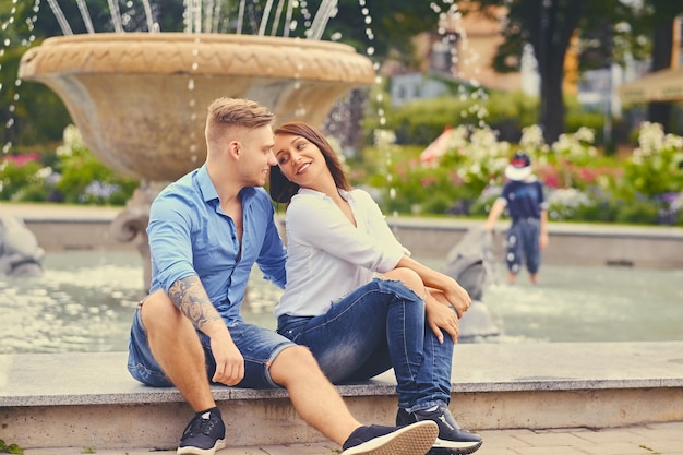 Atractiva pareja moderna en una cita está posando sobre la fuente de la ciudad.
