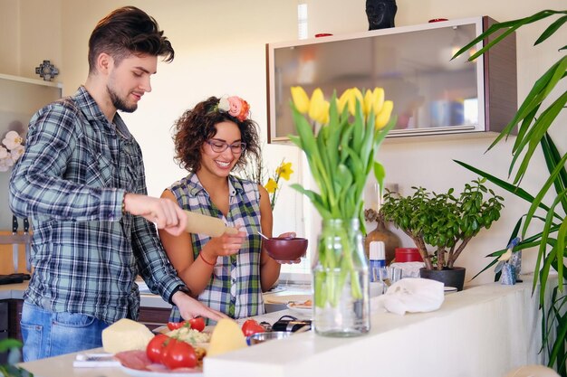 Atractiva pareja de mujeres morenas y un hombre con camisa de lana cocinando la comida en una cocina familiar.