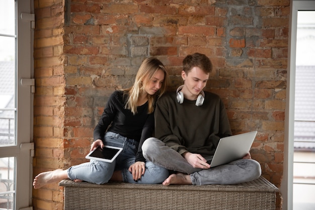 Atractiva pareja sorprendida y asombrada usando dispositivos juntos