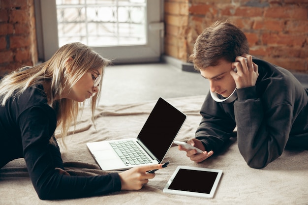 Atractiva pareja sorprendida y asombrada usando dispositivos juntos