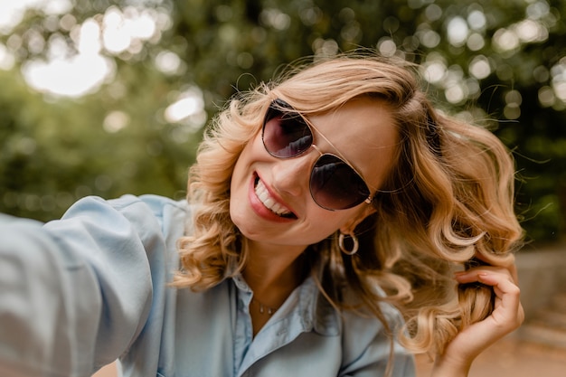 Atractiva rubia sonriente mujer de dientes blancos caminando en el parque en traje de verano tomando foto selfie en teléfono