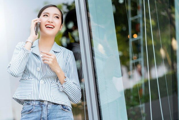 Atractiva sonrisa alegre empresaria asiática smartphone tecnología de comunicación edificio jardín ubicación al aire libre copysapce gratis