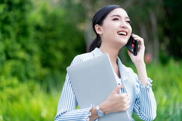 Atractiva sonrisa alegre mujer asiática empresaria portátil connectin tecnología de la comunicación edificio jardín ubicación al aire libre copysapce gratis