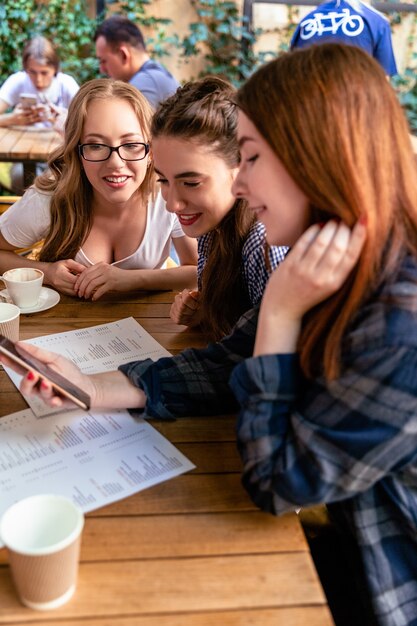 Atractivas chicas jóvenes están mirando la cara frontal de un teléfono inteligente moderno en el café y sonriendo