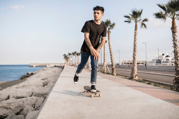 Atractivo adolescente skateboarding cerca de la costa