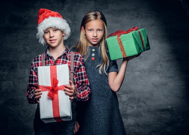 Atractivo adolescente con sombrero de Papá Noel y linda chica rubia tiene cajas de regalo de Navidad.