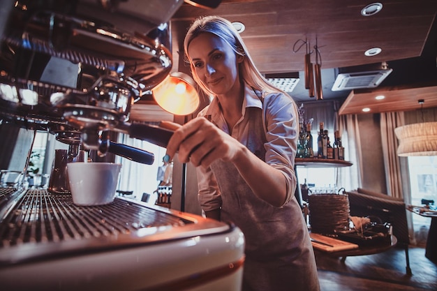 Atractivo barista en uniforme está preparando café para clientes usando una nueva cafetera.