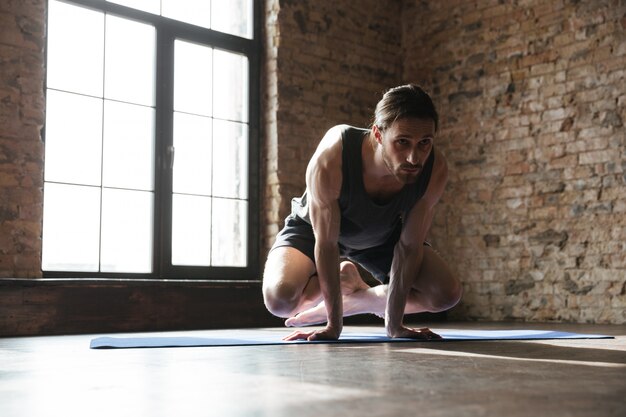 Atractivo deportista fuerte en el gimnasio hacer ejercicios deportivos de yoga