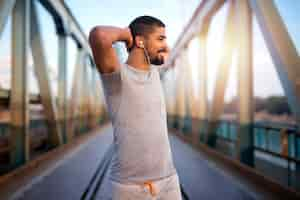 Foto gratuita atractivo deportista sonriente calentando su cuerpo para un entrenamiento al aire libre