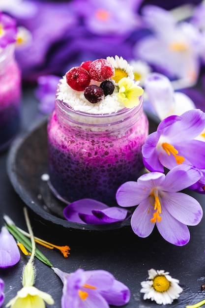 Atractivo frasco de licuado vegano morado cubierto con bayas, rodeado de flores de primavera