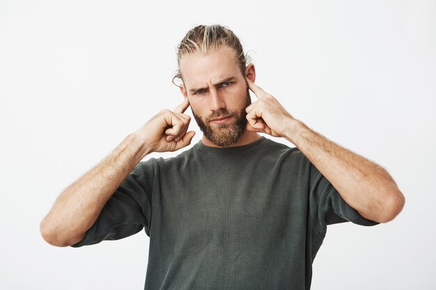 Atractivo hombre barbudo serio cubriendo sus oídos