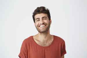 Foto gratuita atractivo hombre joven sin afeitar de piel oscura en camiseta roja ampliamente sonriendo riéndose de la imagen divertida en internet. expresiones faciales positivas y emociones