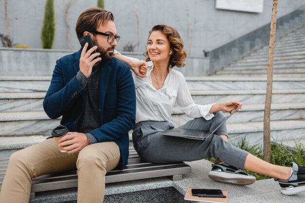 Atractivo hombre y mujer sonriente hablando por teléfono sentado en las escaleras