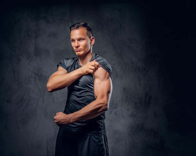 Un atractivo hombre musculoso vestido con ropa deportiva muestra sus músculos en un fondo gris.