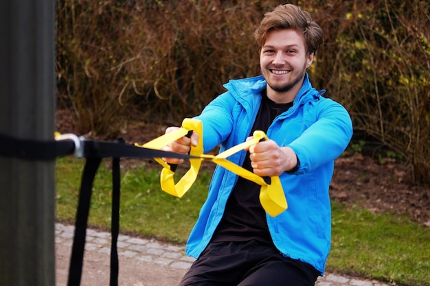 Atractivo hombre positivo haciendo ejercicio con tiras de fitness trx.