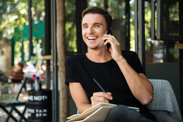 Atractivo hombre riendo hablando por teléfono móvil mientras está sentado