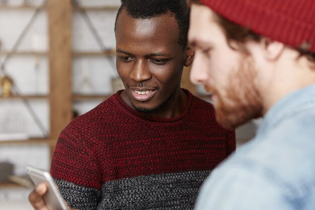 Atractivo joven afroamericano en acogedor suéter con teléfono móvil