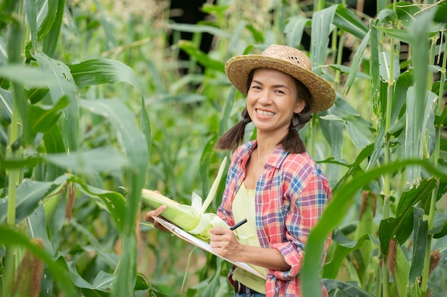 Atractivo joven agricultor sonriendo de pie en el campo de maíz en primavera