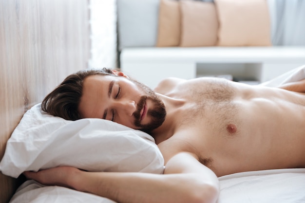 Atractivo joven barbudo durmiendo en la cama