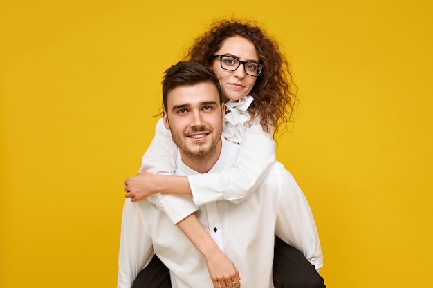 atractivo joven con cerdas dando piggyride a su adorable novia en vasos. Elegante mujer cabalgando sobre la espalda de su novio, sonriendo felizmente. Citas y relaciones