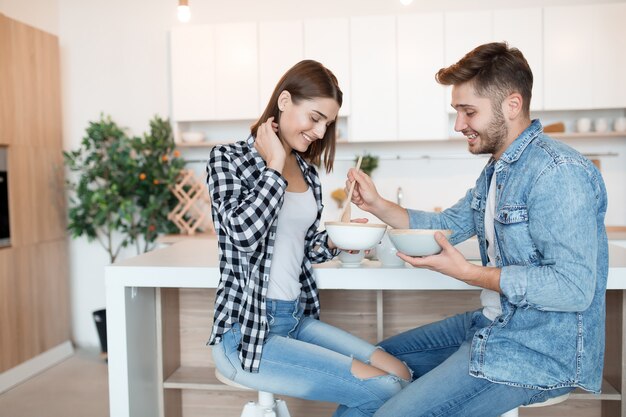 Atractivo joven feliz y mujer en la cocina, desayunando, pareja juntos en la mañana, sonriendo