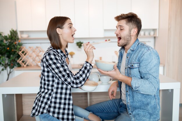 Atractivo joven feliz y mujer en la cocina, desayunando, pareja juntos en la mañana, sonriendo