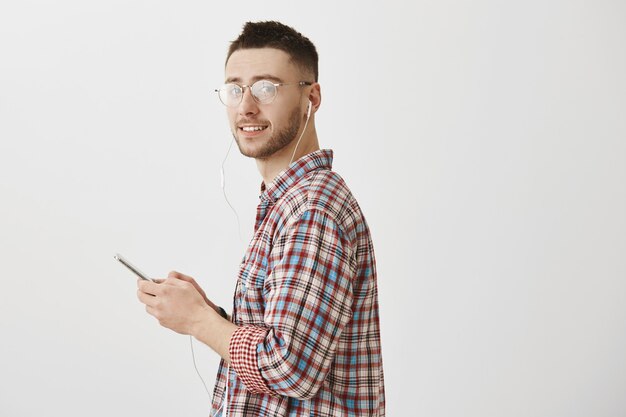 atractivo joven con gafas posando con su teléfono y auriculares