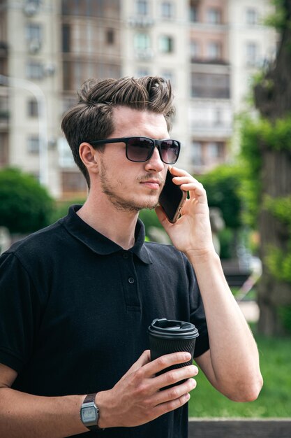 Atractivo joven con gafas de sol hablando por un teléfono inteligente en la ciudad