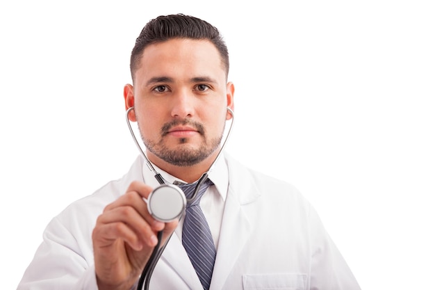 Atractivo joven médico con barba usando un estetoscopio para examinar a un paciente contra un fondo blanco