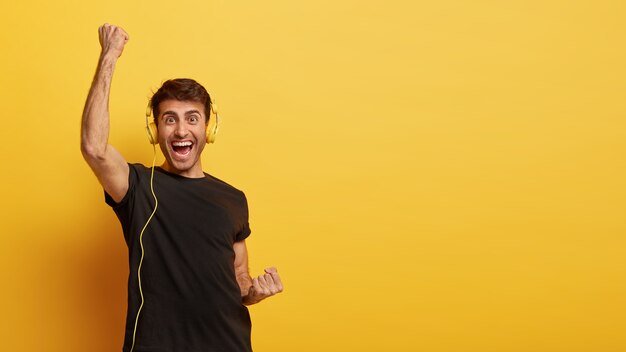 Atractivo joven se siente feliz y lleno de alegría, levanta los puños cerrados