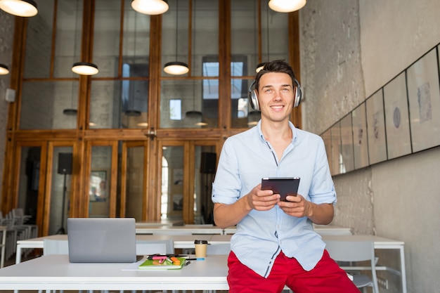 Atractivo joven sonriente feliz con tableta escuchando música en auriculares inalámbricos