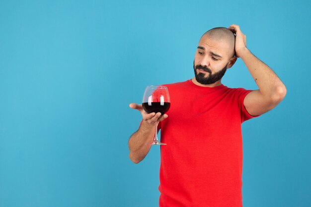 Atractivo joven sosteniendo una copa de vino tinto contra la pared azul.