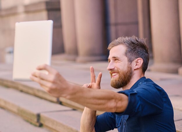 El atractivo macho barbudo haciendo selfie en un tablet PC.