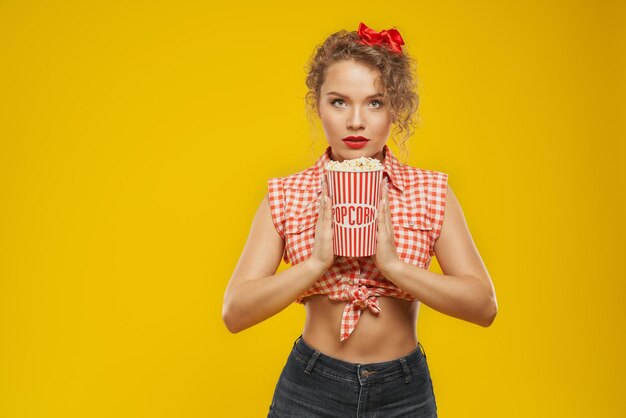 Atractivo modelo pin up que muestra un cubo de palomitas de maíz