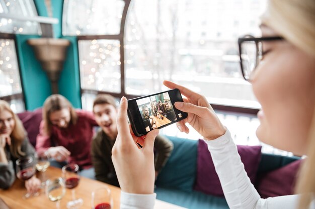 Atractivos amigos sentados en la cafetería y hacer fotos por teléfono.