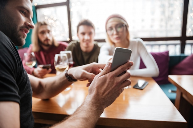 Atractivos amigos sentados en la cafetería y mirando el teléfono.