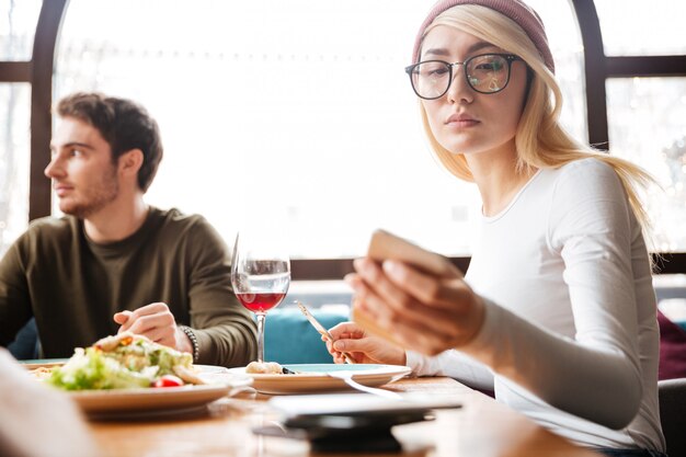 Atractivos amigos sentados en la cafetería. Mujer usando su teléfono móvil.