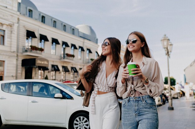 Atractivos modelos elegantes caminando con un café hablando, diviértase en la ciudad de fondo