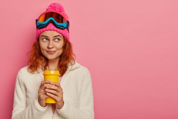 Attractve mujer pelirroja lleva gorro, gafas de esquí y jersey blanco