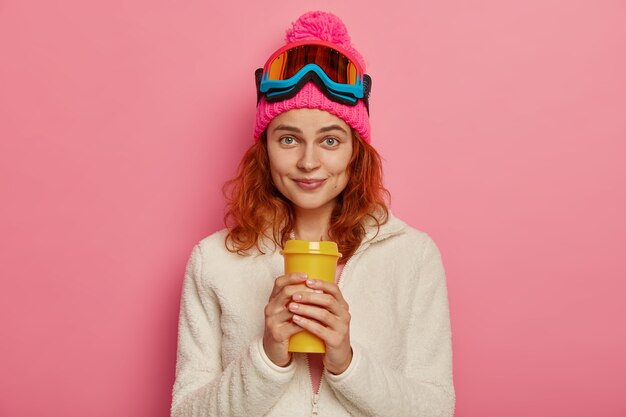 Attractve mujer pelirroja lleva gorro, gafas de esquí y jersey blanco