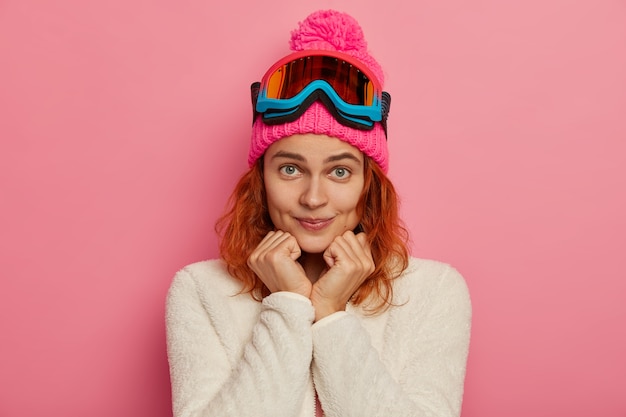 Attractve mujer pelirroja lleva gorro, gafas de esquí y jersey blanco