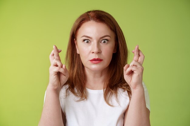 Aturdida intensa preocupada mujer pelirroja de mediana edad mirar nerviosamente esperando resultado importante implorar sueño hecho realidad recibir respuesta positiva estupor de pie pared verde pedir deseo buena suerte